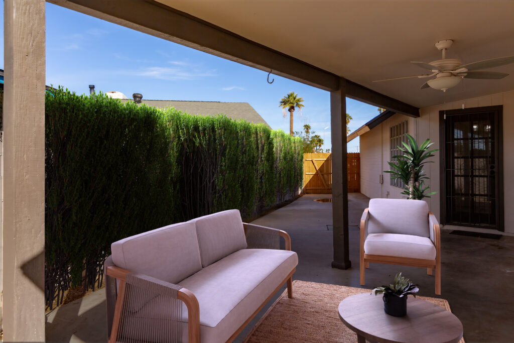 Side patio with hedge against wall with neighbors and patio furniture and potted plant. All digitally staged.